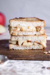 Two halves of brie grilled cheese with apples, stacked on a wooden board.