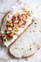 Assembling a brie grilled cheese with apples, showing bread topped with melted brie and diced apples.