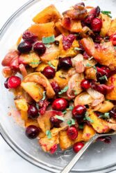 Roast pumpkin with maple syrup, cranberries, and apples in a clear glass bowl.