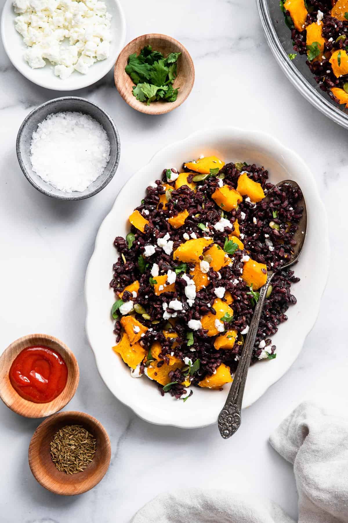 Harvest Black Rice Salad - This easy rice salad is topped with roasted pumpkin, harissa, and goat cheese for a delicious, flavorful, gluten free and healthy fall meal! Perfect for a side dish or meatless dinner! | #foodfaithfitness | #glutenfree #vegetarian #healthy #sidedish a wild rice salad in a bowl with ingredients in bowls around it