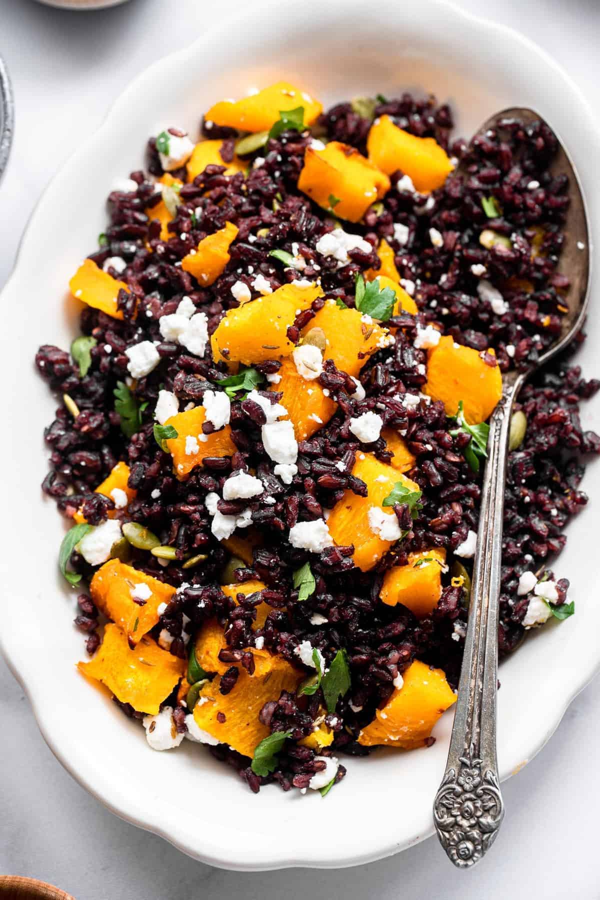 Harvest Black Rice Salad - This easy rice salad is topped with roasted pumpkin, harissa, and goat cheese for a delicious, flavorful, gluten free and healthy fall meal! Perfect for a side dish or meatless dinner! | #foodfaithfitness | #glutenfree #vegetarian #healthy #sidedish roasted pumpkin and black rice salad in a bowl with a spoon