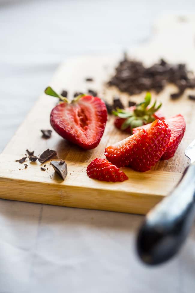 Banana Split Vegan Smoothie Bowl - This vegan smoothie bowl is made with only 5 ingredients, ready in 5 minutes, tastes like a banana split, and is secretly healthy enough for breakfast! | #Foodfaithfitness | #Glutenfree #Vegan #Healthy #paleo #dairyfree strawberries on a cutting board with chocolate for vegan smoothie bowl