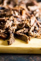Shredded slow-cooker roast beef on a wooden cutting board.