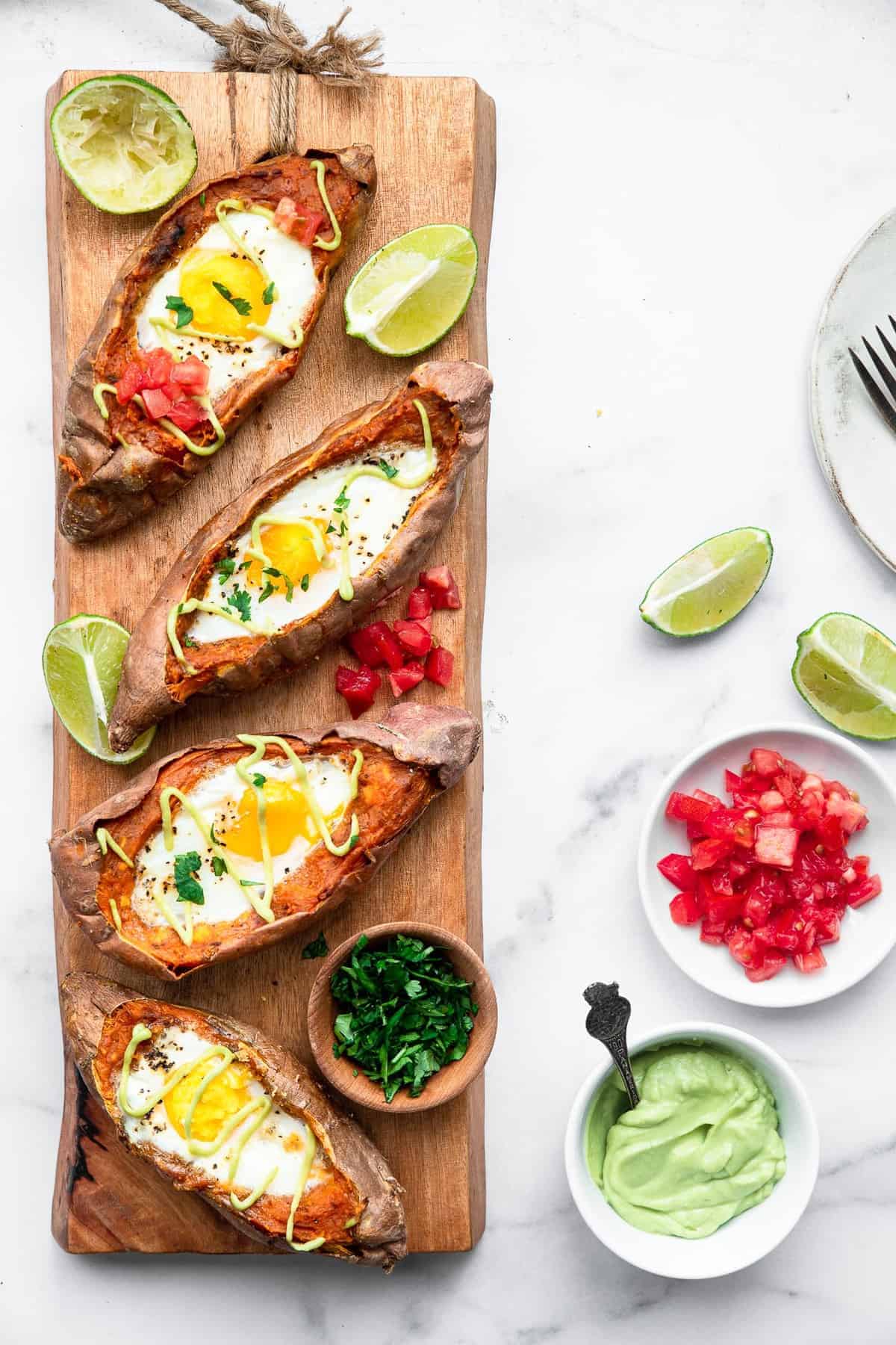 Twice Baked Mexican Sweet Potatoes - These Twice Baked Mexican Sweet Potatoes have a runny egg and a tangy lime avocado sauce! They're a healthy, gluten free and whole30 meal! | #Foodfaithfitness | #glutenfree #paleo #whole30 #healthy 4 Mexican Stuffed Sweet Potatoes on a cutting board