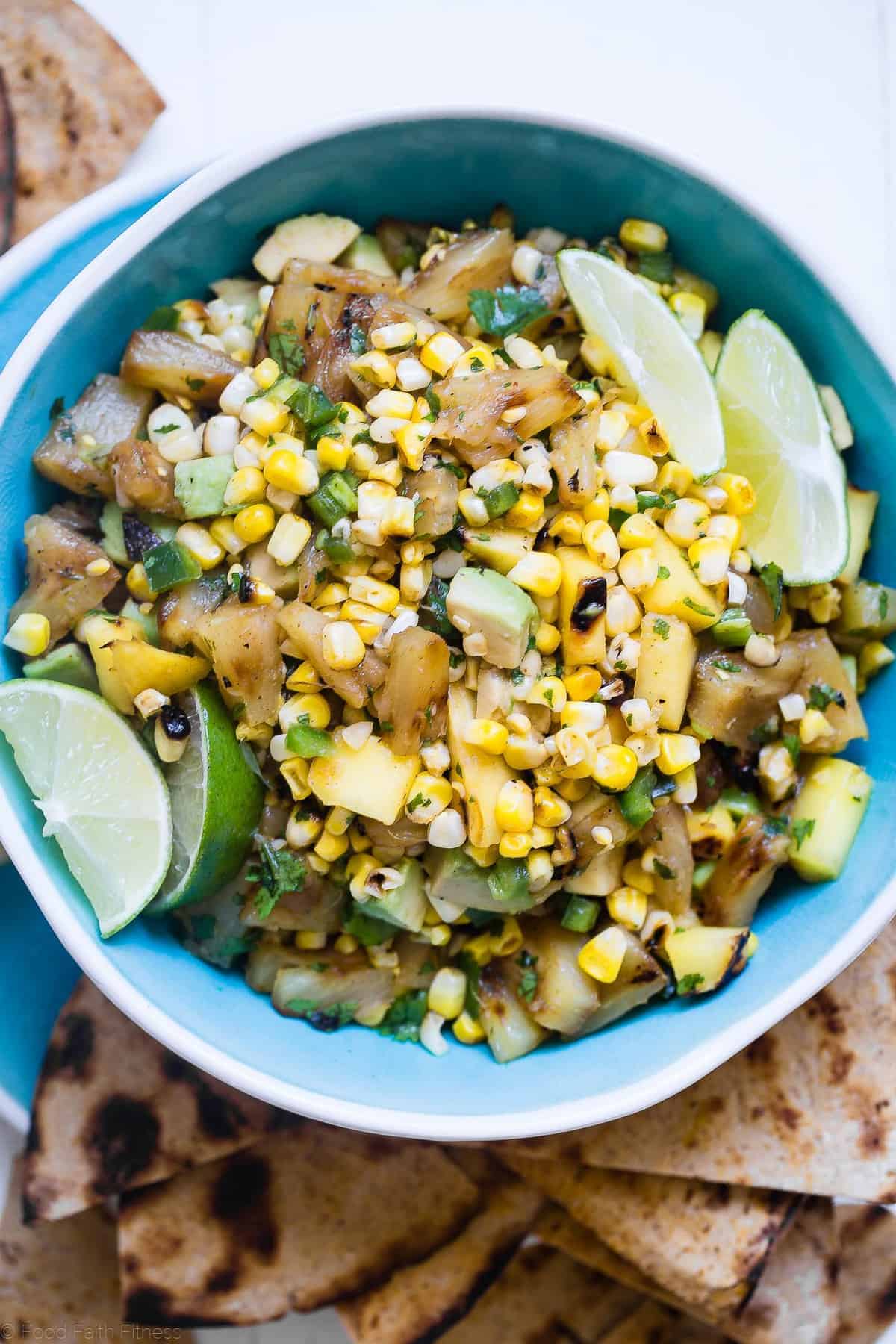 Tropical Grilled Corn Salsa - This quick and easy grilled pineapple mango salsa is mixed with corn and a honey lime vinaigrette for an a healthy, gluten free and vegan-friendly summer appetizer or dinner! | #Foodfaithfitness | #glutenfree #salsa #corn #healthy extreme close up of salsa in a blue bowl with lemons and limes