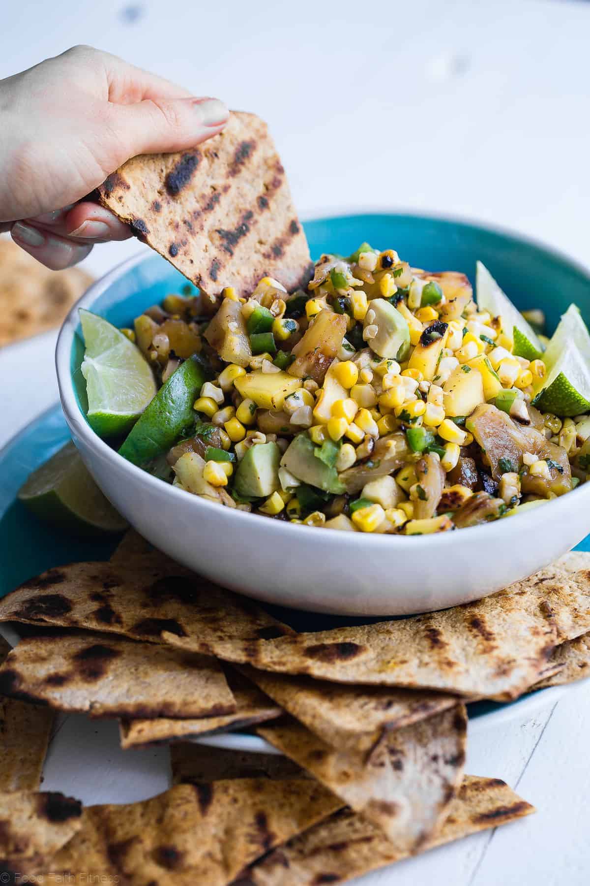Tropical Grilled Corn Salsa - This quick and easy grilled pineapple mango salsa is mixed with corn and a honey lime vinaigrette for an a healthy, gluten free and vegan-friendly summer appetizer or dinner! | #Foodfaithfitness | #glutenfree #salsa #corn #healthy grilled chips being dipped into pineapple mango salsa