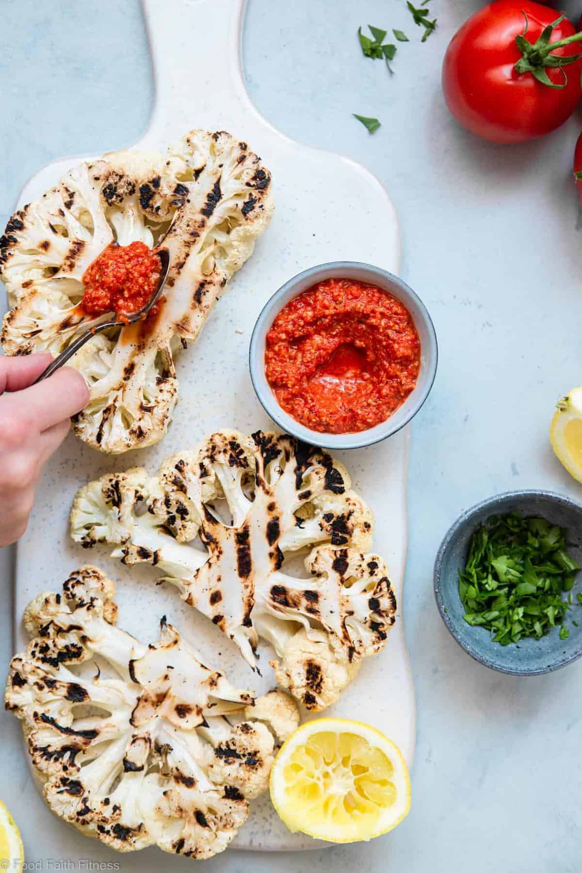 A hand spreading sauce on cauliflower steak on the grill