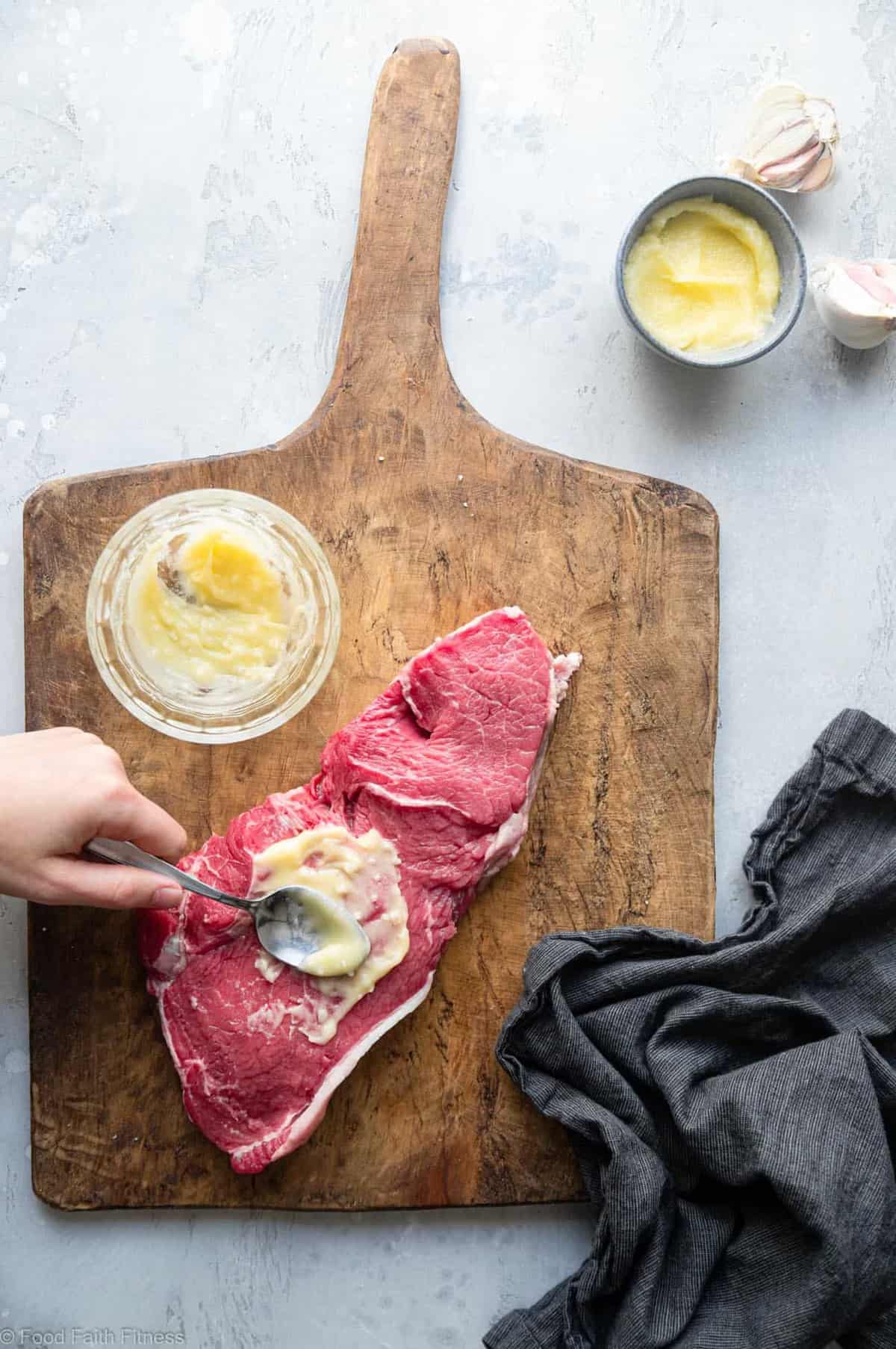 Keto Steak with Garlic Butter Mushrooms - This keto steak recipe is topped with garlic butter mushrooms and grilled to perfection! A low carb, paleo and whole30 healthy Summer dinner! | #Foodfaithfitness | #Glutenfree #Paleo #Keto #Lowcarb #whole30 spreading butter onto raw steak on a cutting board