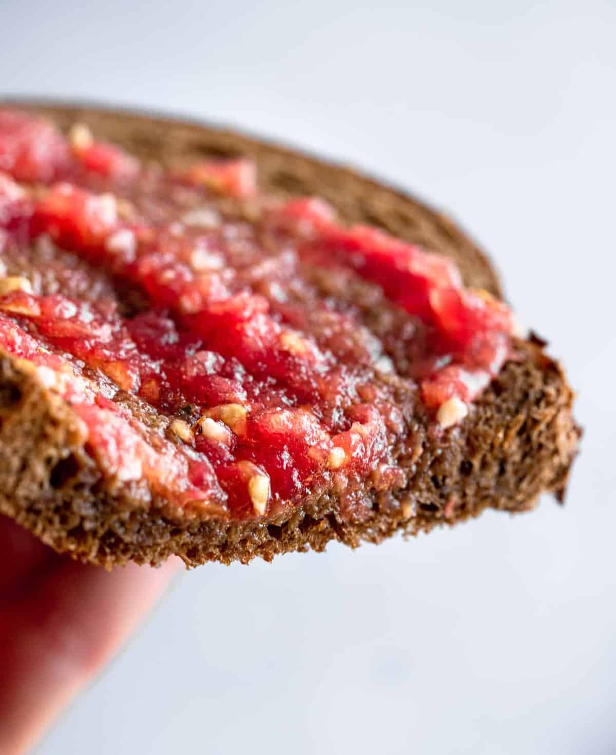 Pan Con Tomate - Tomato toast is a traditional Spanish breakfast that is made from 4 simple, healthy ingredients and has big flavor! This will be your new go to breakfast! Naturally Paleo, low carb and vegan too! | #Foodfaithfitness | #Glutenfree #Paleo #Lowcarb #Vegan #sugarfree close up of hand holding pan con tomate