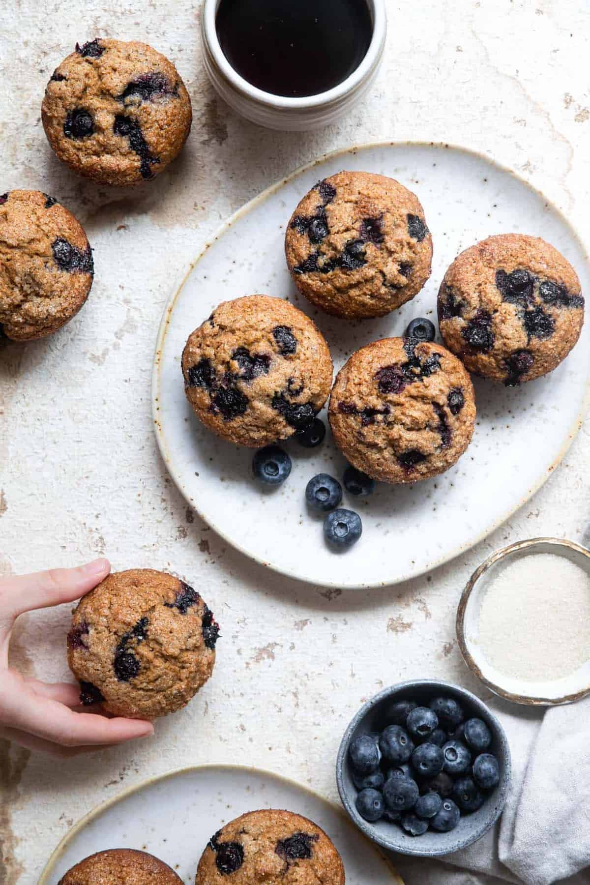 whole wheat blueberry muffins on a plate with a hand grabbing one