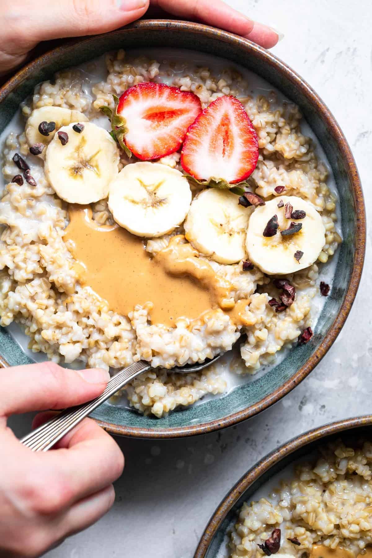 Instant Pot Steel Cut Oats - a quick, simple breakfast that are only 2 ingredients! Naturally gluten free, vegan, healthy and SO filling! Great for meal prep too! | #Foodfaithfitness | #Glutenfree #vegan #healthy #sugarfree #dairyfree #Instantpot close up of a hand scooping a bowl of instant pot steel cut oats