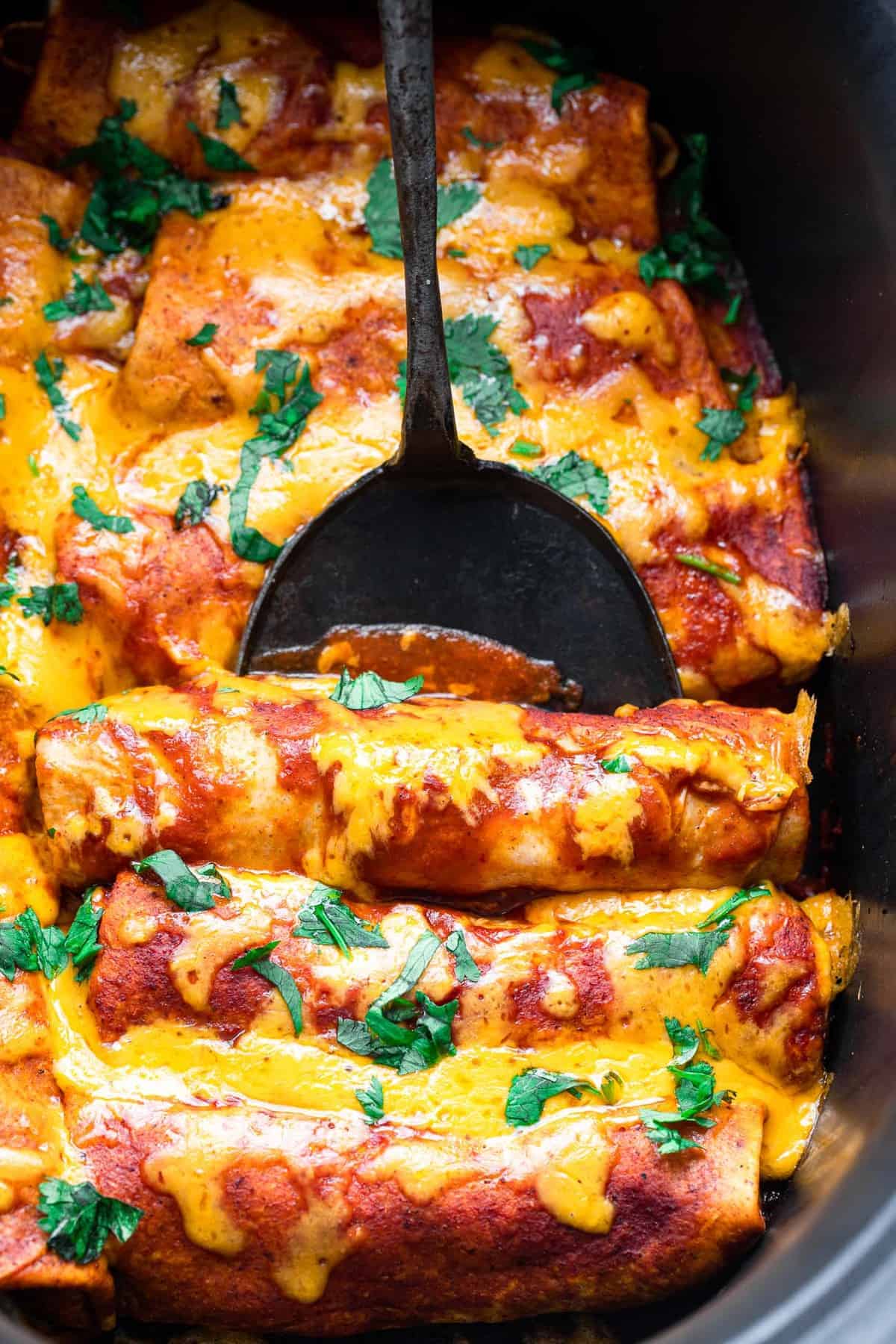 Healthy Crock Pot Chicken Enchiladas - an easy, healthy weeknight dinner that the whole family will love - even picky eaters! Makes great leftovers and freezer meals too! | #Foodfaithfitness | #healthy #dinner #slowcooker #crockpot #kidfriendly a serving spoon with crock pot chicken enchiladas on it