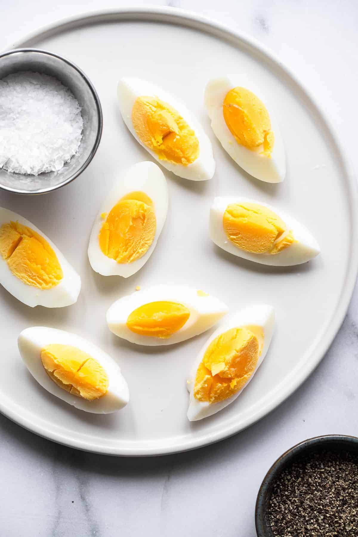 Air Fryer Hard Boiled Eggs - These 1 ingredient air fryer hard boiled eggs are even easier than boiling them and come out perfect every time! Gluten free, keto, paleo, low carb and healthy! The perfect snack or addition to a meal! | #Foodfaithfitness | #airfryer #glutenfree #keto #paleo #lowcarb sliced air fryer hard boiled eggs on a plate with a bowl of salt
