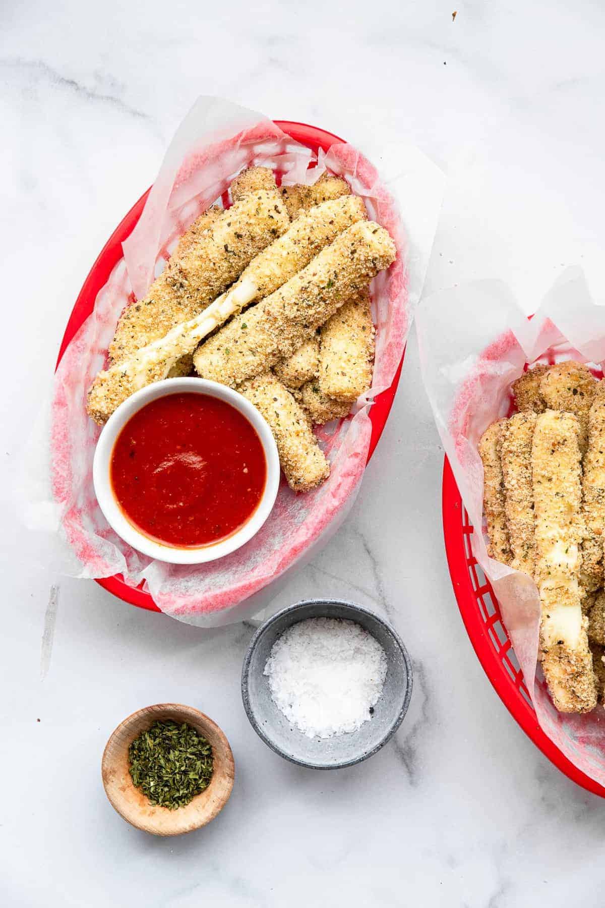 Crispy Oven Baked Mozzarella Sticks - This Oven Baked Mozzarella Sticks Recipe is SO crispy and gooey, you will never believe they are baked, not fried, and only 5 ingredients! | #Foodfaithfitness | #glutenfree #healthy #appetizer #gameday two bowls of oven baked mozzarella sticks with marinara sauce
