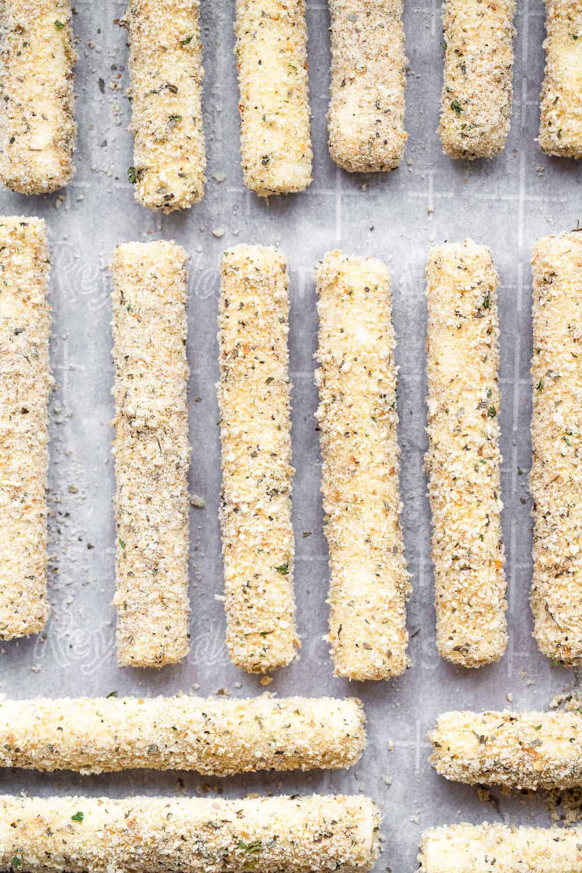 Crispy Oven Baked Mozzarella Sticks - This Oven Baked Mozzarella Sticks Recipe is SO crispy and gooey, you will never believe they are baked, not fried, and only 5 ingredients! | #Foodfaithfitness | #glutenfree #healthy #appetizer #gameday baked cheese sticks lined up on a baking sheet
