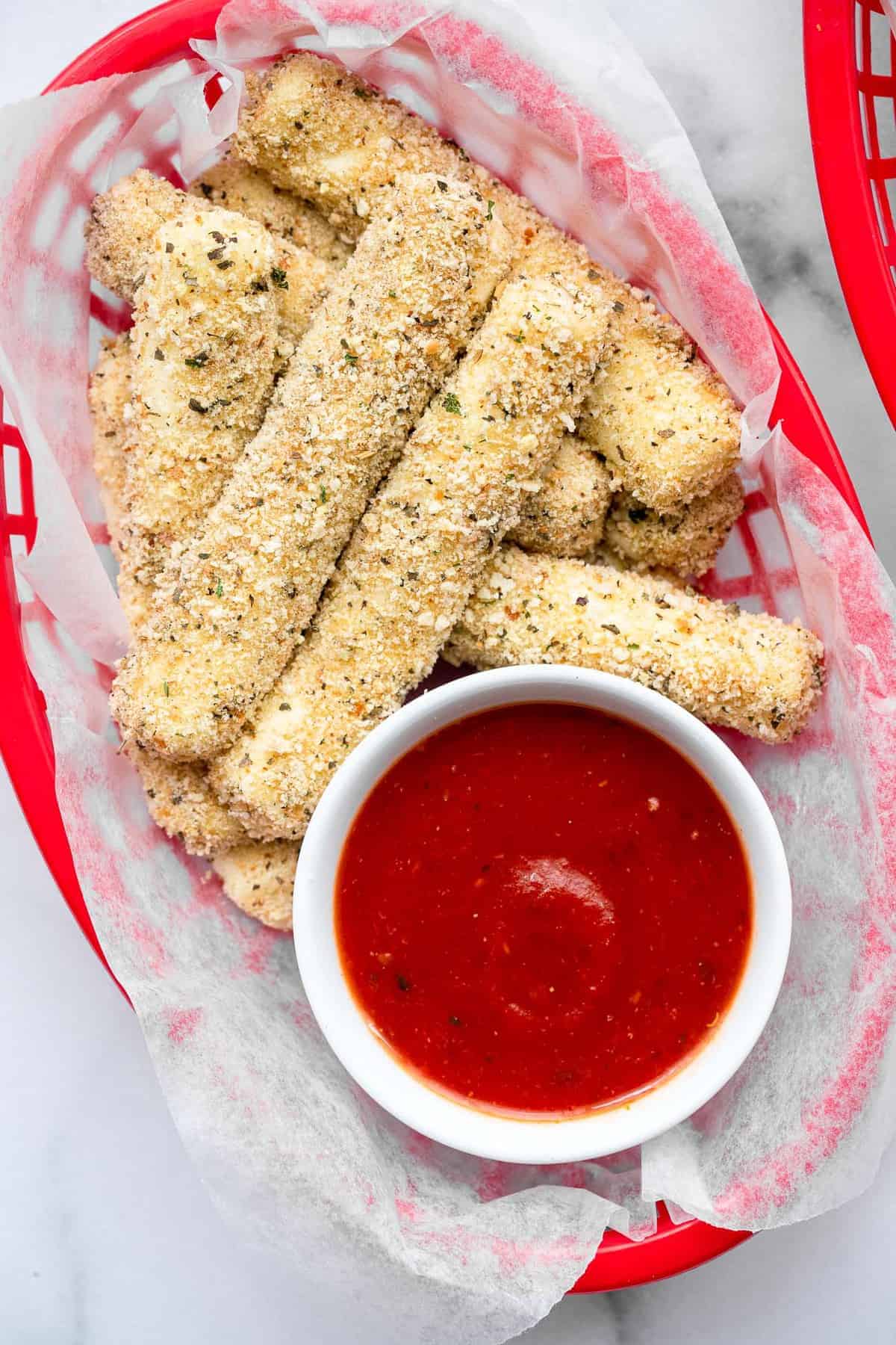 Crispy Oven Baked Mozzarella Sticks - This Oven Baked Mozzarella Sticks Recipe is SO crispy and gooey, you will never believe they are baked, not fried, and only 5 ingredients! | #Foodfaithfitness | #glutenfree #healthy #appetizer #gameday baked mozzarella cheese sticks in a bowl with marinara sauce