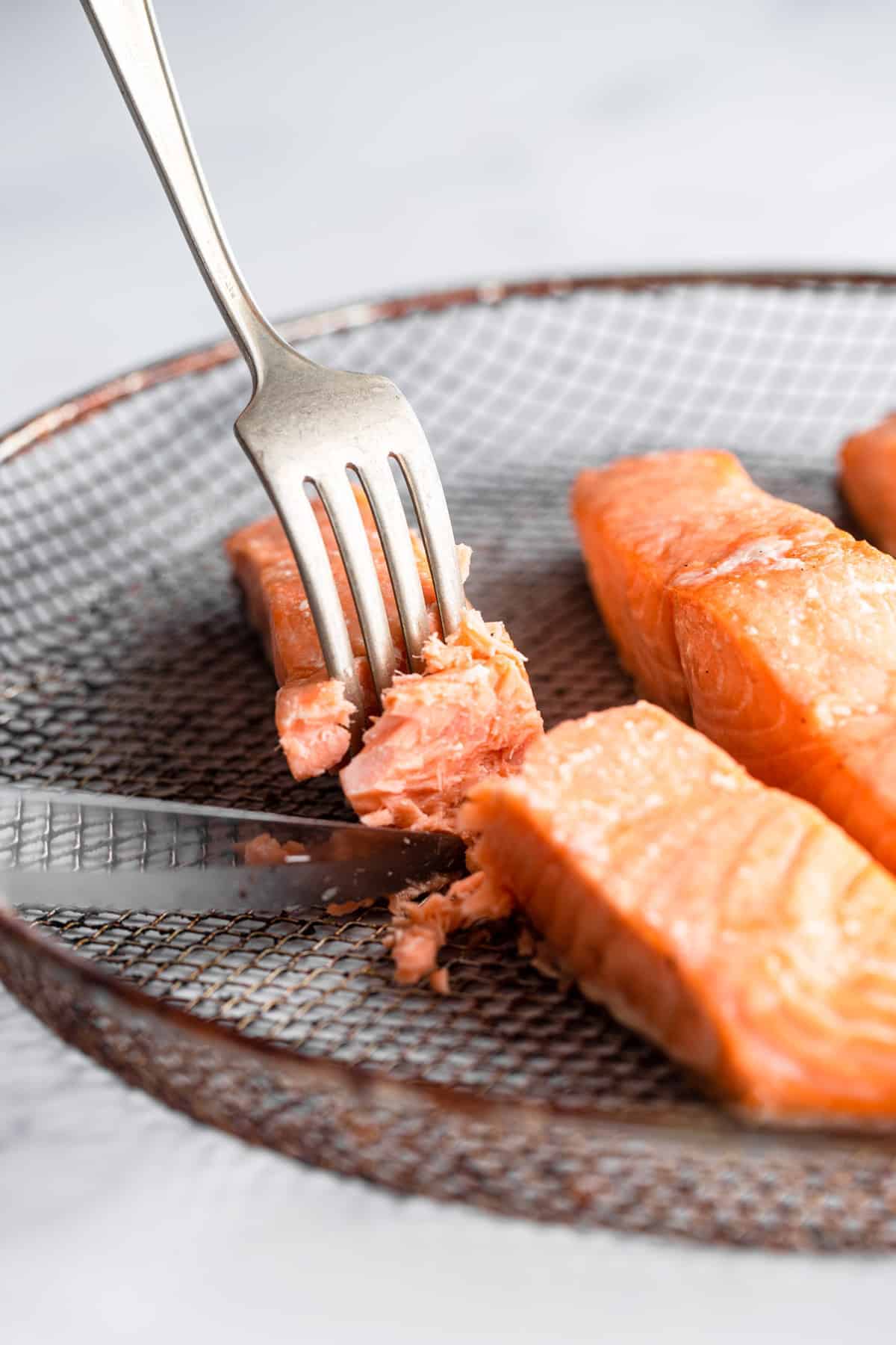 air fryer salmon cooked on a mesh plate with fork and knife