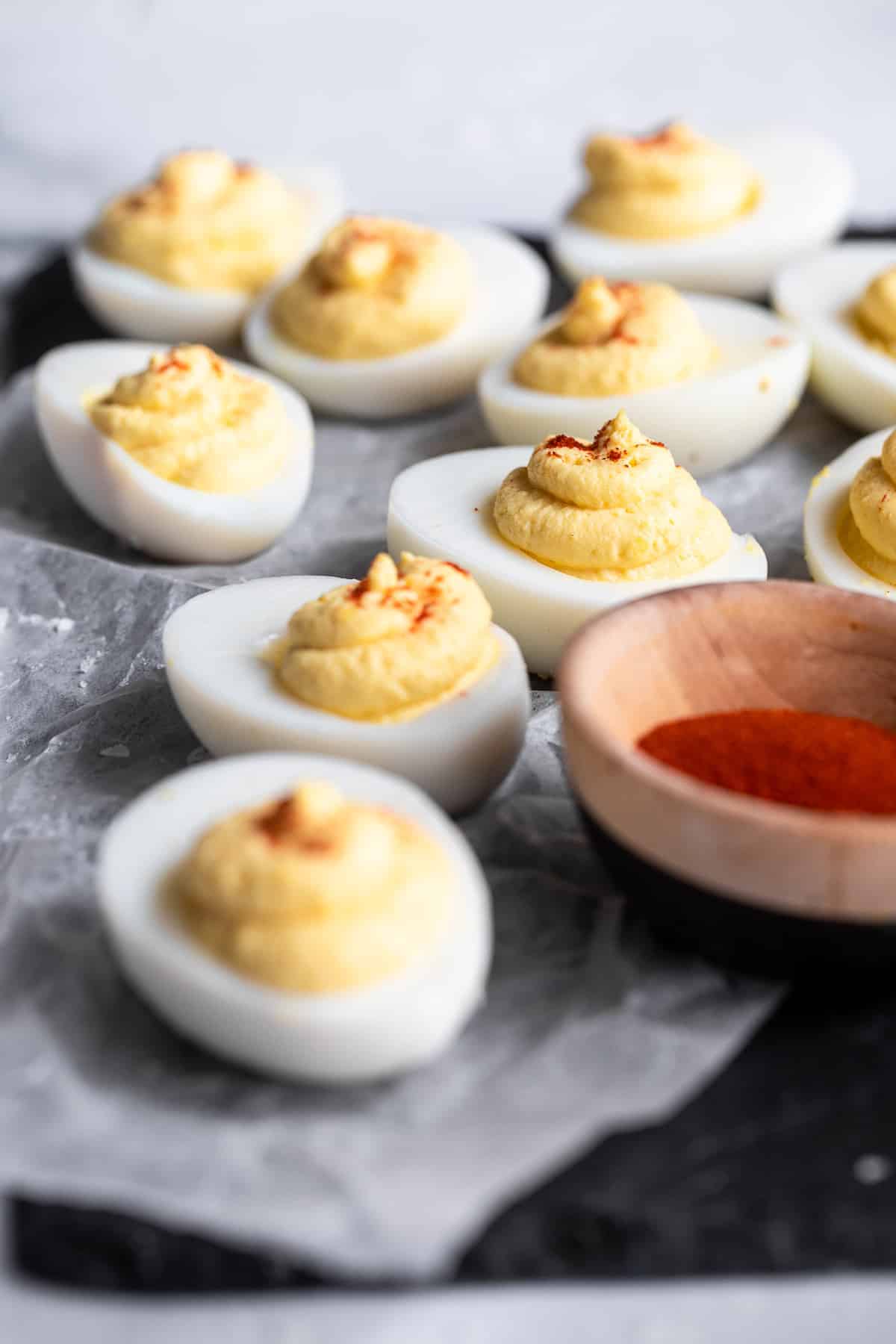 Greek Yogurt Healthy Deviled Eggs - These Healthy Deviled Eggs with Greek Yogurt are only 4 ingredients, low carb, keto friendly and packed with protein! An easy, crowd-pleasing recipe! You will never know they have no mayo! | #Foodfaithfitness | #glutenfree #keto #lowcarb #Greekyogurt #healthy Deviled Eggs on parchment paper with paprika