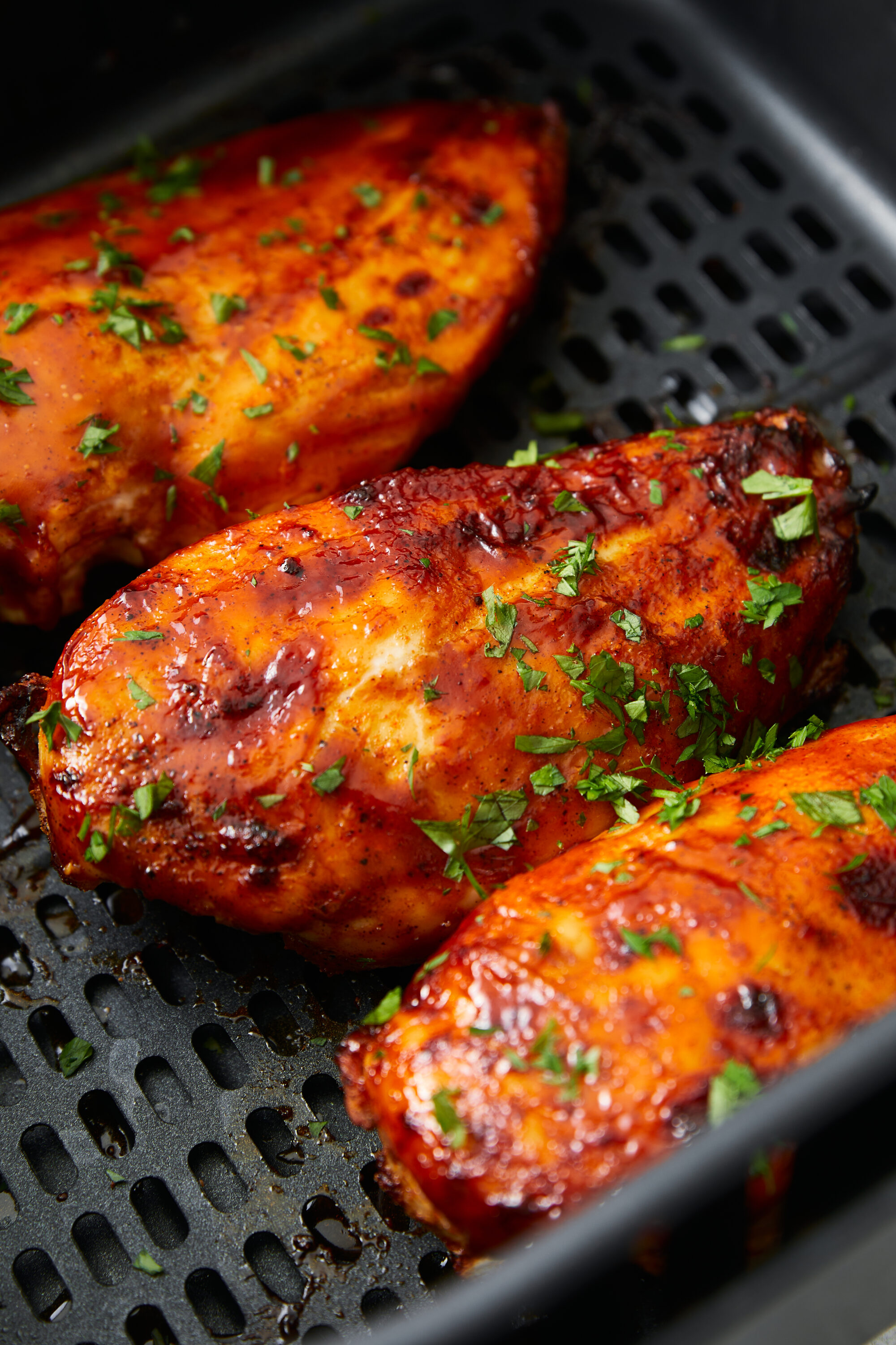 Three air-fried BBQ chicken breasts, coated in sauce and garnished with fresh herbs.