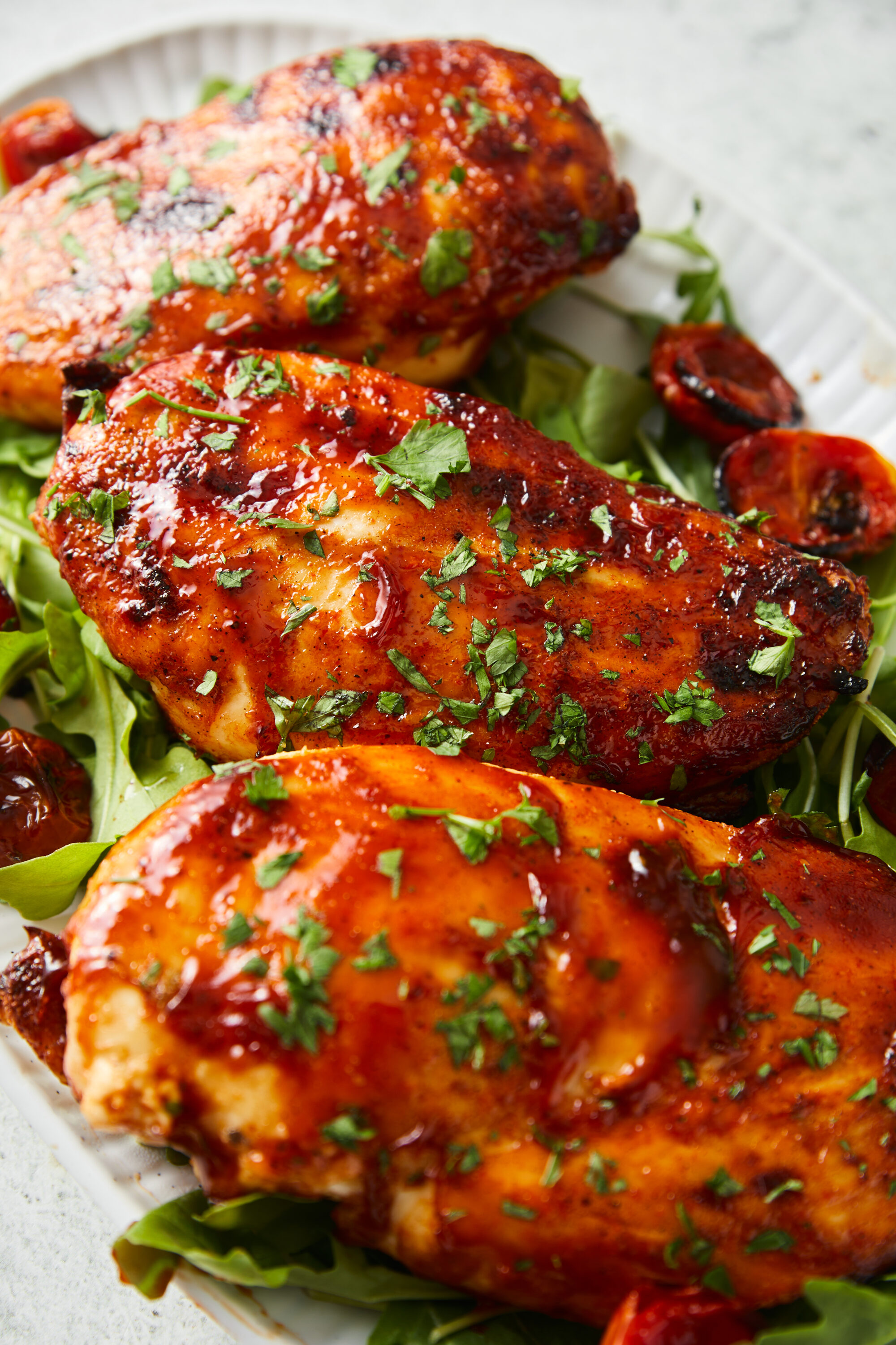 Three air-fried BBQ chicken breasts, glazed with sauce and garnished with herbs, served on arugula.