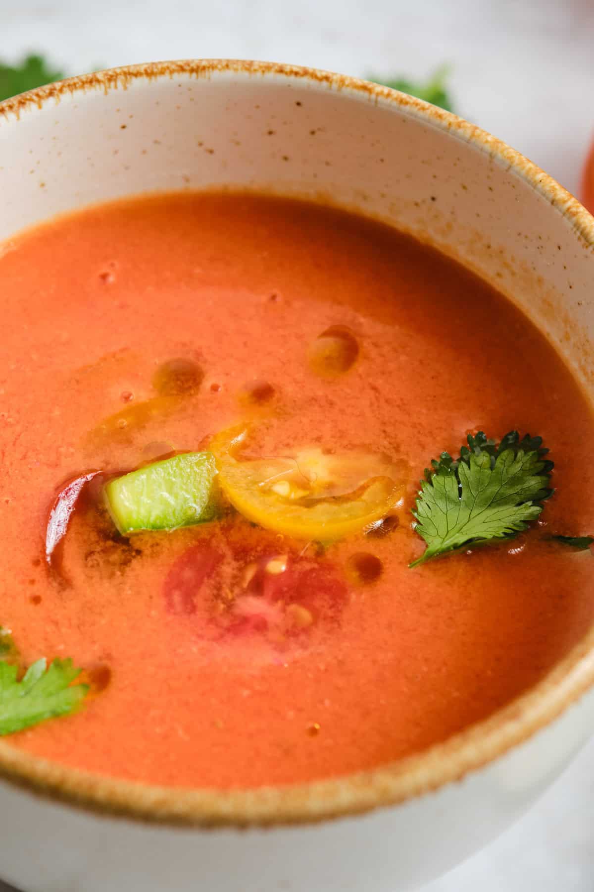A bowl of gazpacho garnished with sliced cherry tomatoes, green bell pepper, cilantro, and olive oil.