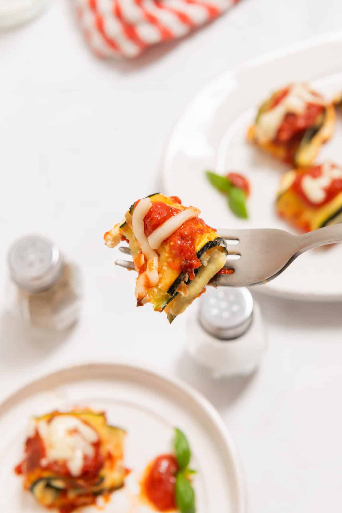 A zucchini lasagna roll on a fork, topped with red sauce and melted cheese.