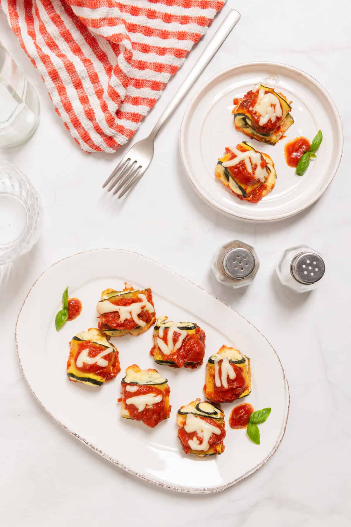 Zucchini lasagna rolls topped with red sauce, melted cheese, and fresh basil on white plates.