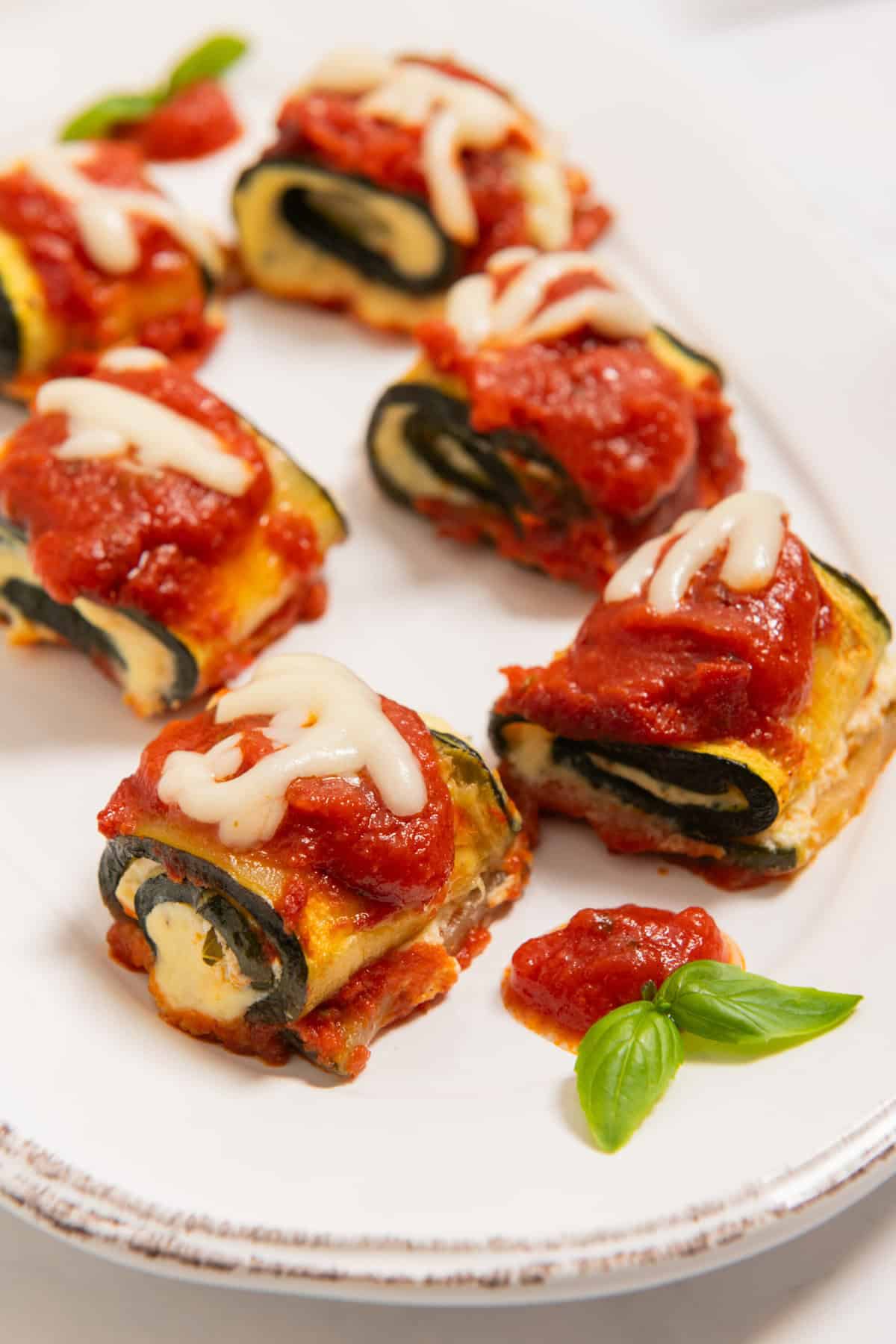 Zucchini lasagna rolls on a white plate, topped with marinara sauce and melted cheese.
