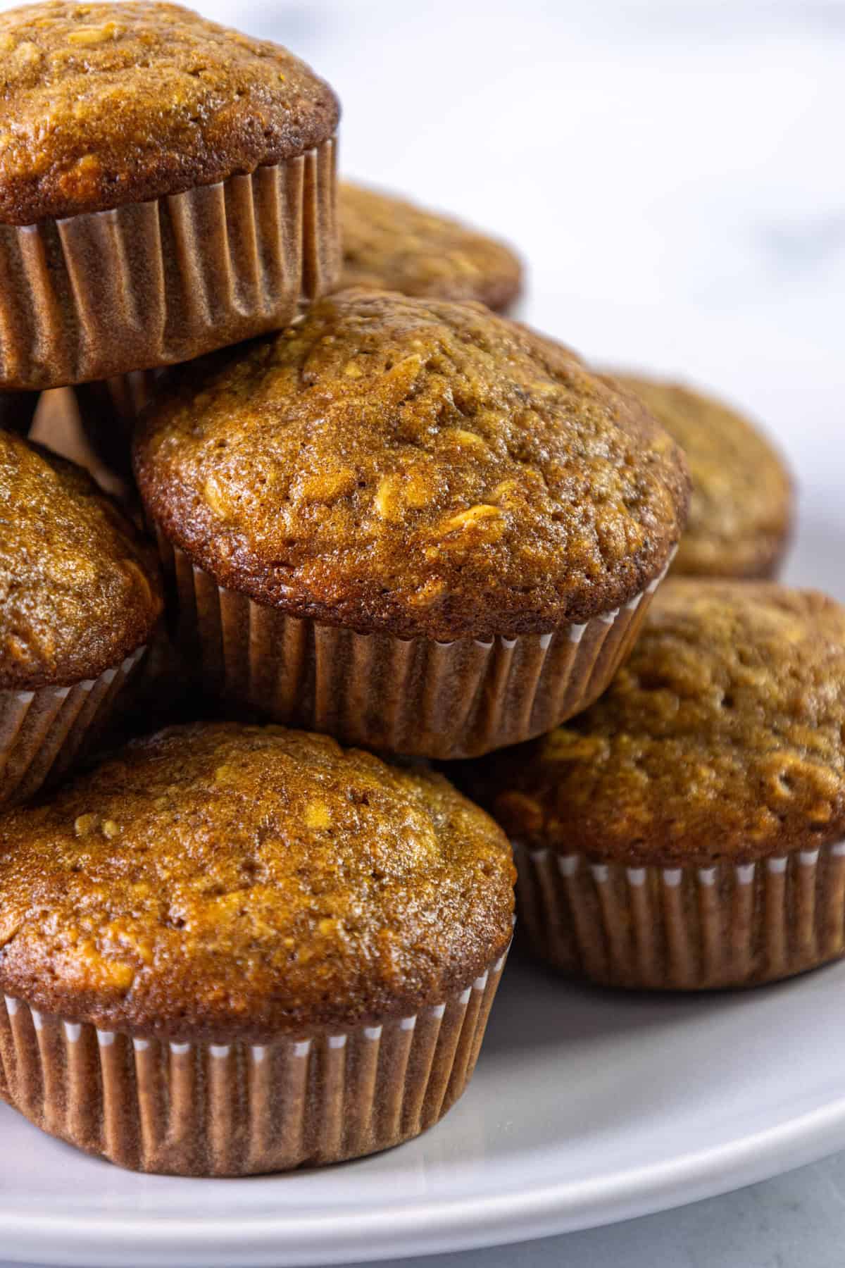 A pile of golden brown oatmeal muffins in paper liners on a white plate.