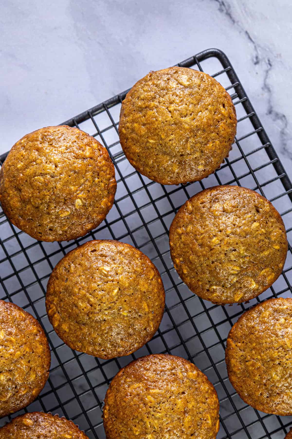 Oatmeal muffins cooling on a black wire rack, showing their golden-brown tops with visible oats.