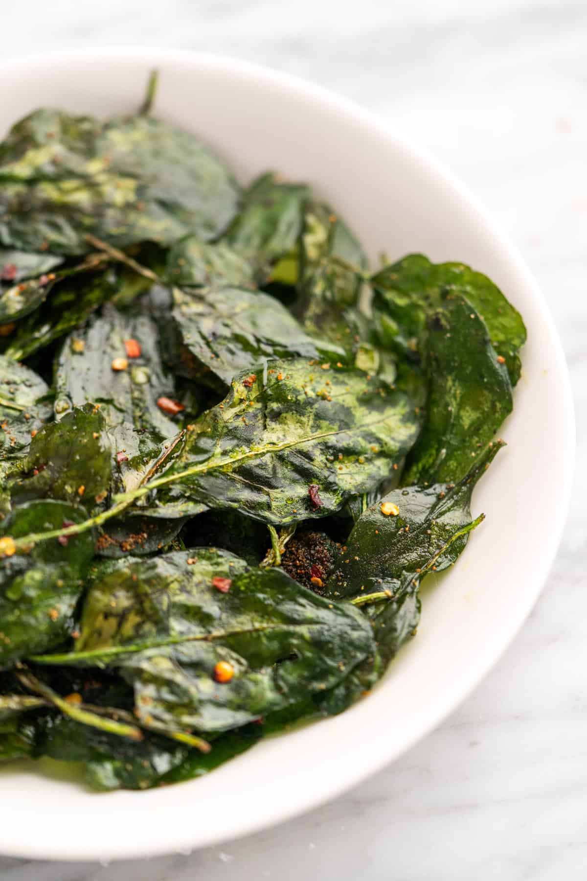 Spinach chips in a white bowl, seasoned with red pepper flakes and spices.