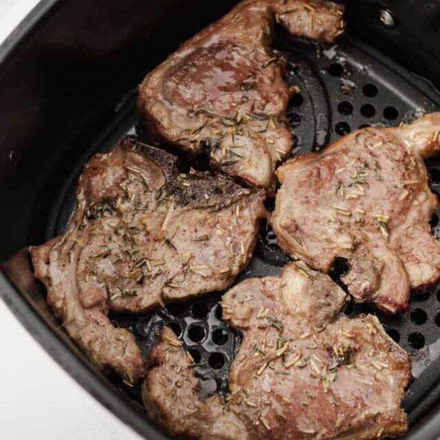 Juicy, seasoned steaks cooking in an air fryer, topped with herbs for a healthy, delicious meal. Perfect for balanced eating and easy meal prep.