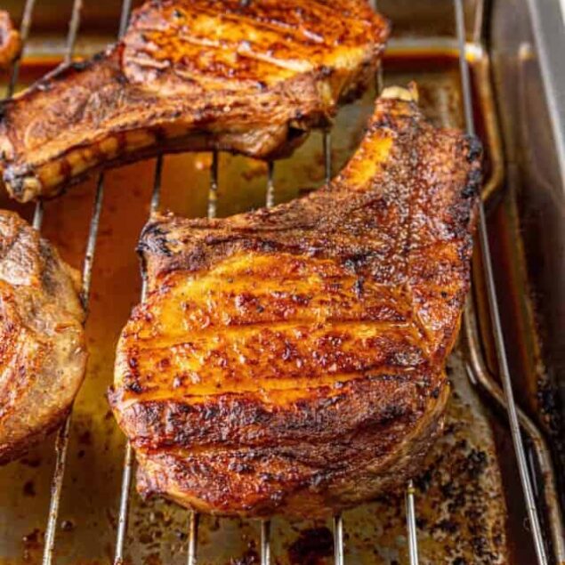 Succulent oven-cooked bone-in pork chops on a baking rack, showcasing golden-brown, flavorful grilled meat perfect for healthy, high-protein meal prep and delicious dinner options.