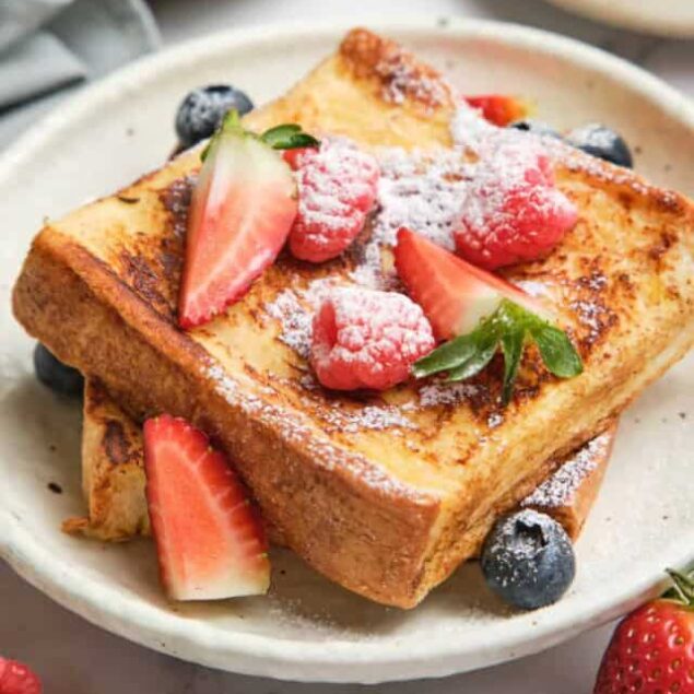 Fluffy French toast topped with fresh strawberries, raspberries, blueberries, and powdered sugar, served on a white plate, perfect for a healthy breakfast or brunch.