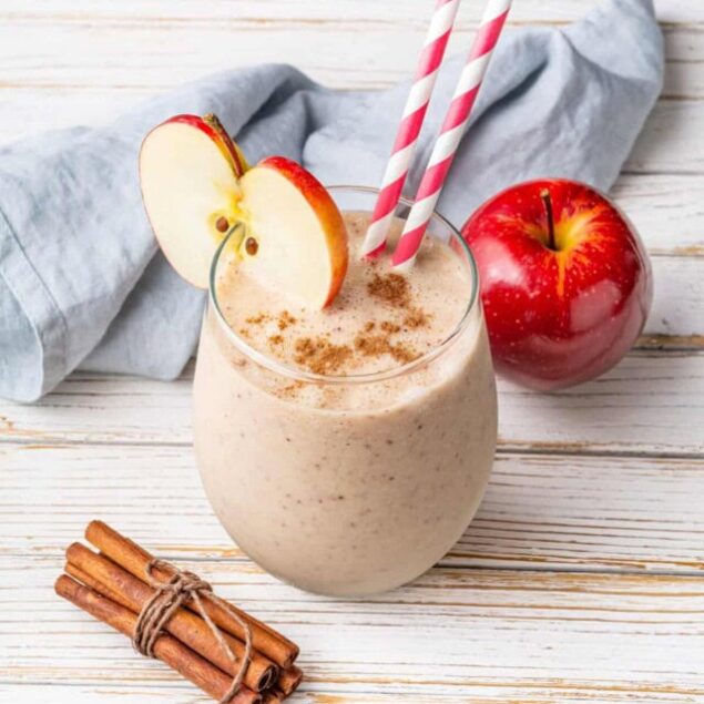 Creamy apple cinnamon smoothie with fresh apple slices and cinnamon sticks on a rustic wooden table.