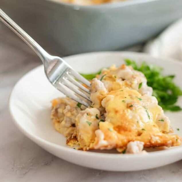 Crispy baked chicken casserole with melted cheese and fresh herbs on white plate.