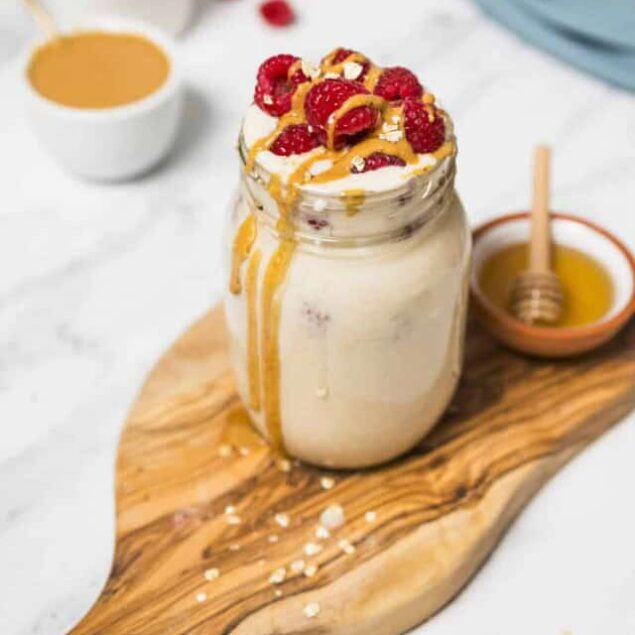 Creamy smoothie jar topped with fresh raspberries and a drizzle of honey, served on a wooden board with a honey dipper and bowls of fruit compote, highlighting healthy, nutritious recipes from Food Faith Fitness.