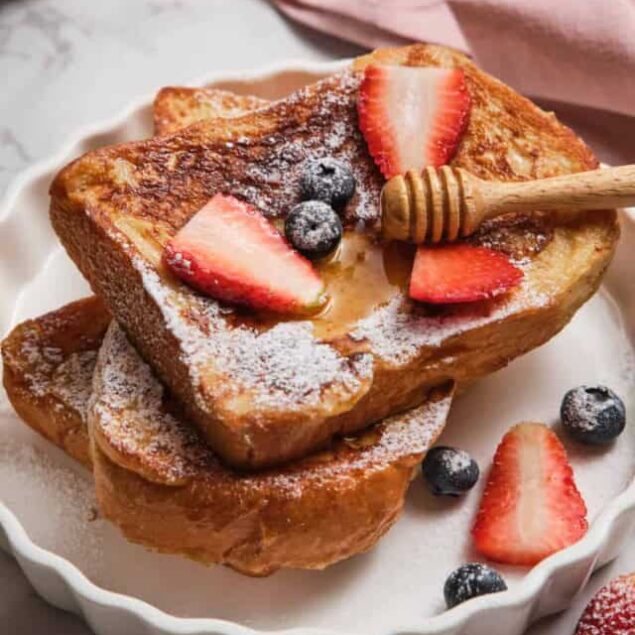 Sweet French Toast Sticks topped with fresh strawberries and blueberries, drizzled with honey and dusted with powdered sugar. Perfect for a healthy breakfast or brunch.