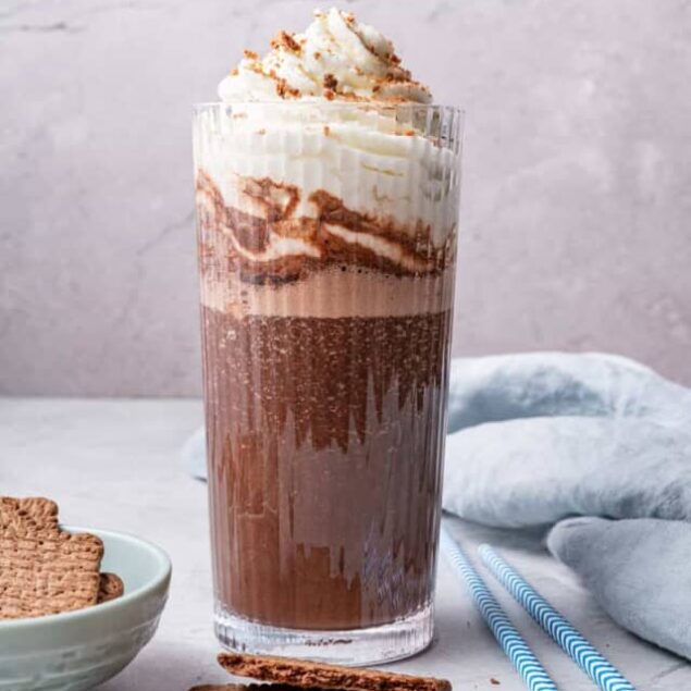 Rich chocolate milkshake with whipped cream and cocoa powder in a tall glass, garnished with chocolate shavings, on a light textured background perfect for indulgent dessert recipes and healthy eating inspiration.
