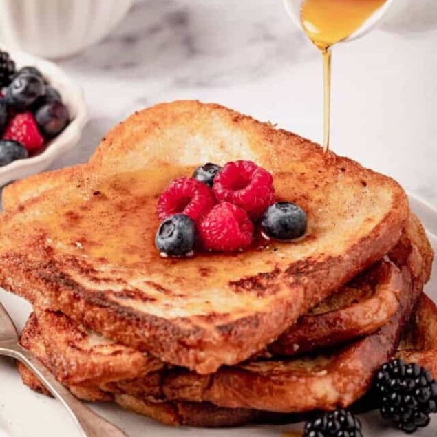 Golden brown French toast stacked with fresh berries and drizzled with maple syrup, perfect for a nutritious breakfast.