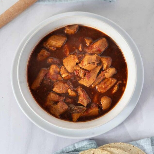 Spicy pork stew in a white bowl with stacked tortillas on a paper towel, perfect for healthy meal prep and flavorful dinners.