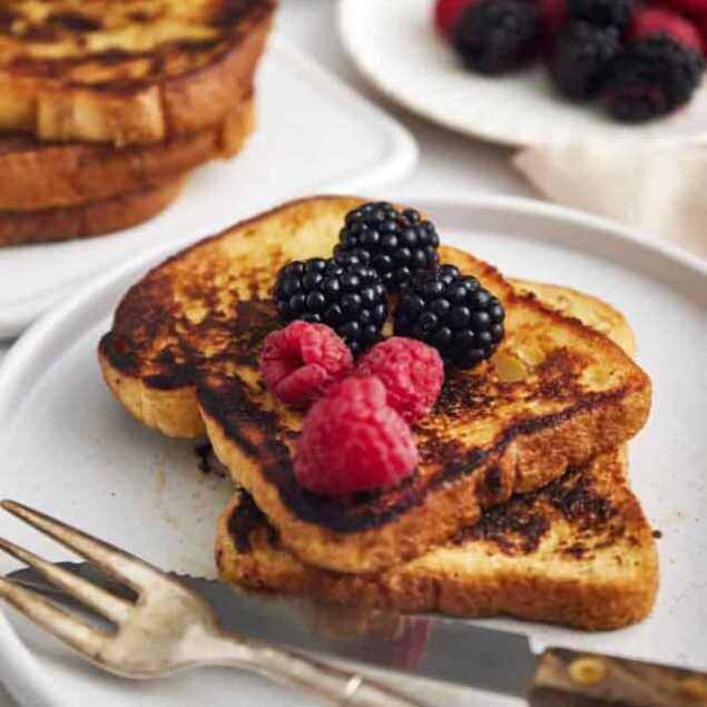 Golden-brown French toast topped with fresh blackberries and raspberries on a white plate. A nutritious breakfast option with berries for added antioxidants and flavor.
