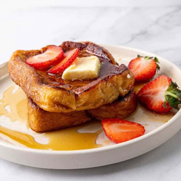 Golden French toast topped with strawberries, butter, and syrup on a white plate, showing a delicious healthy breakfast option from Food Faith Fitness.