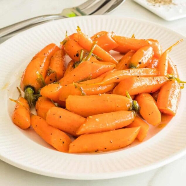 Bright roasted orange carrots on a white plate, garnished with black pepper and herbs, perfect for healthy eating, meal prep, or side dishes.