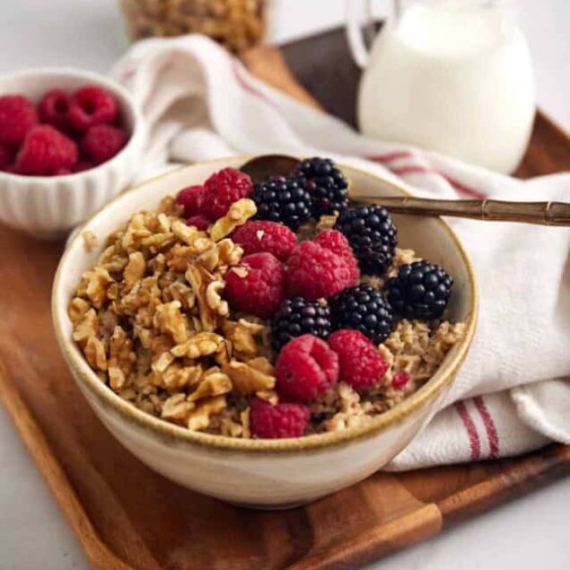 Fresh berry oatmeal bowl with raspberries, blackberries, granola, served on a wooden tray with milk, healthy breakfast, clean eating, nutritious start, food faith fitness.