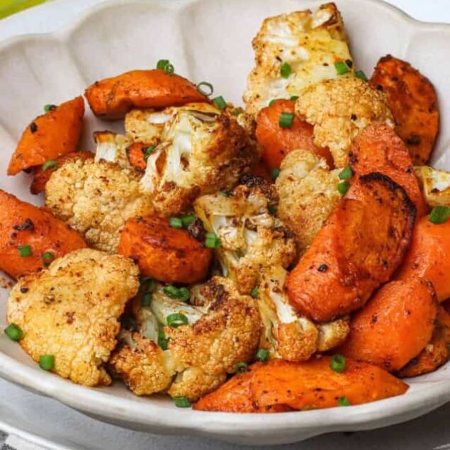 Roasted cauliflower and sweet potatoes with green onions in a white bowl, healthy plant-based roasted vegetable dish.