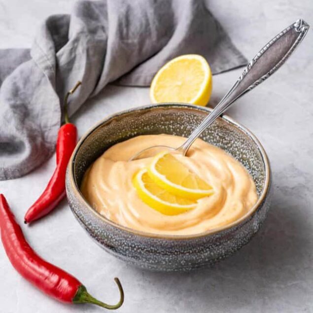 Creamy lemon dip with fresh lemon slices and red chili peppers on a light surface. Perfect for healthy snacks, appetizers, or as a zestful addition to meals. Easy, delicious, and nutritious.