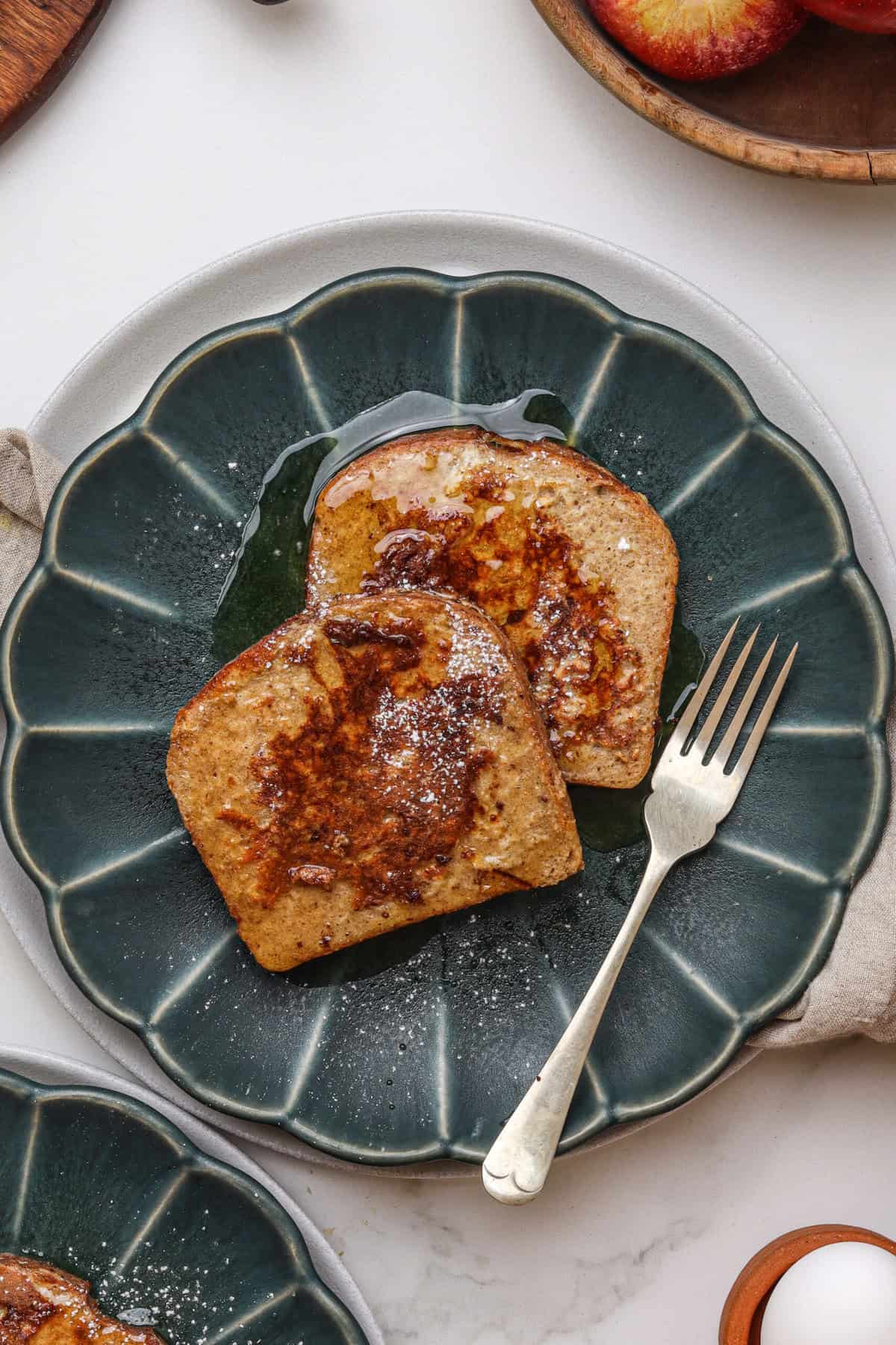 Gluten-free French toast on a dark green plate, drizzled with syrup and powdered sugar.