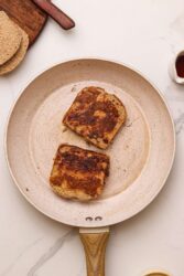 Two pieces of gluten-free French toast browning in a non-stick pan.