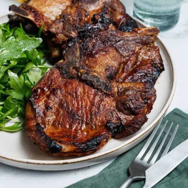 Succulent grilled pork chops with a caramelized exterior served with fresh arugula salad on a white plate. Perfect for healthy, high-protein meals and easy weeknight dinners.